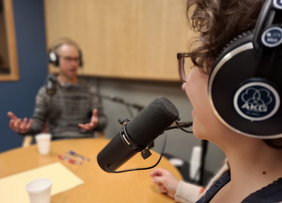 Dame og mann med hodetelefoner som sitter i radiostudio og snakker